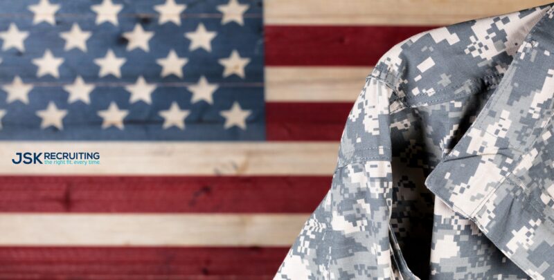 A soldier in fatigues standing next to an american flag.