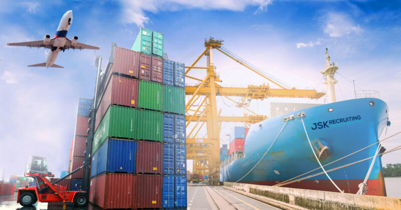 A large cargo ship emblazoned with the JSK Recruiting logo docks next to a stack of shipping containers as a plane flies overhead.