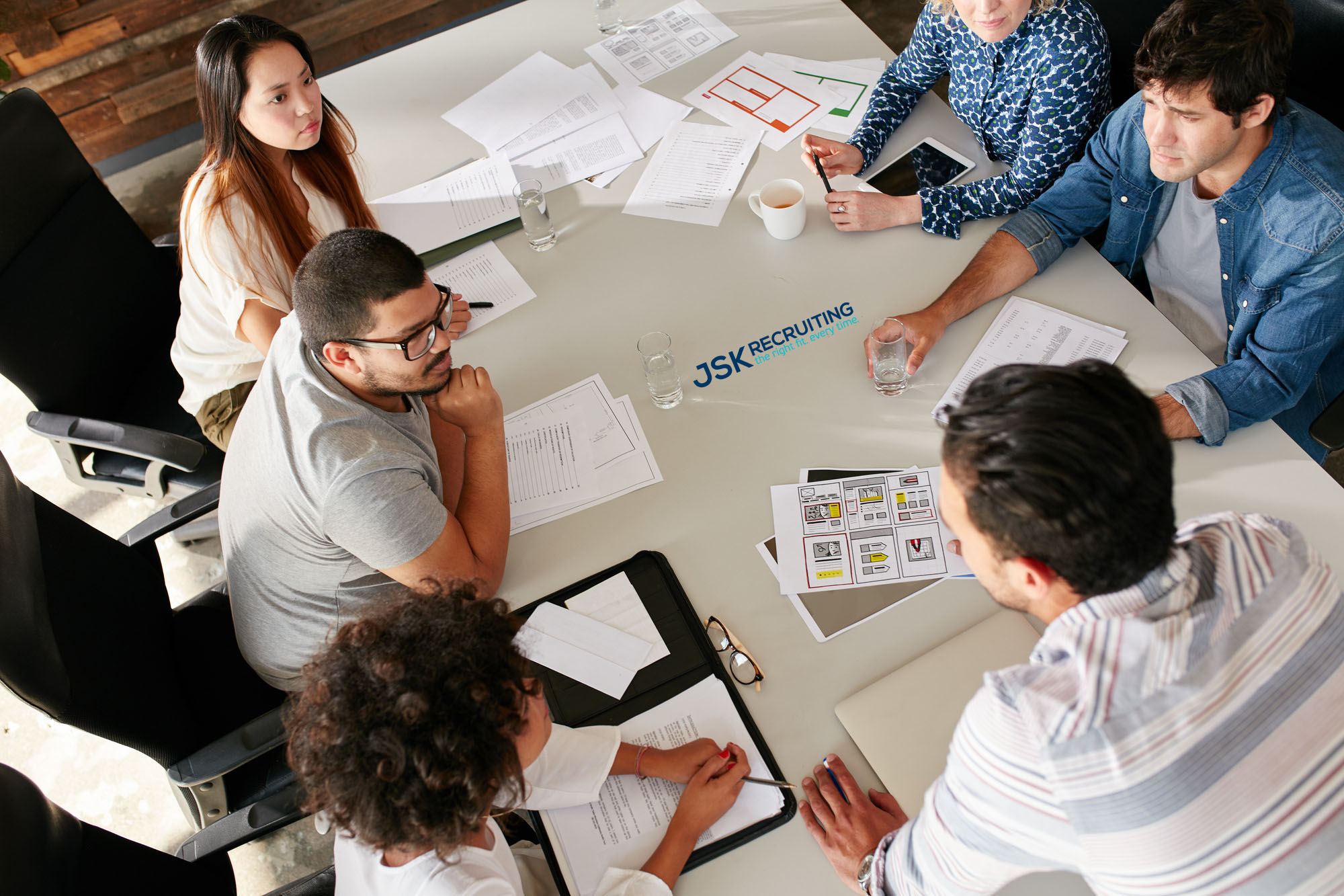 High angle view of creative team sitting around conference table watermarked with the JSK Recruiting logo discussing business ideas.