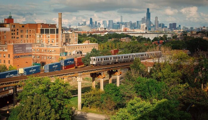 A train is traveling over the bridge in front of a city.