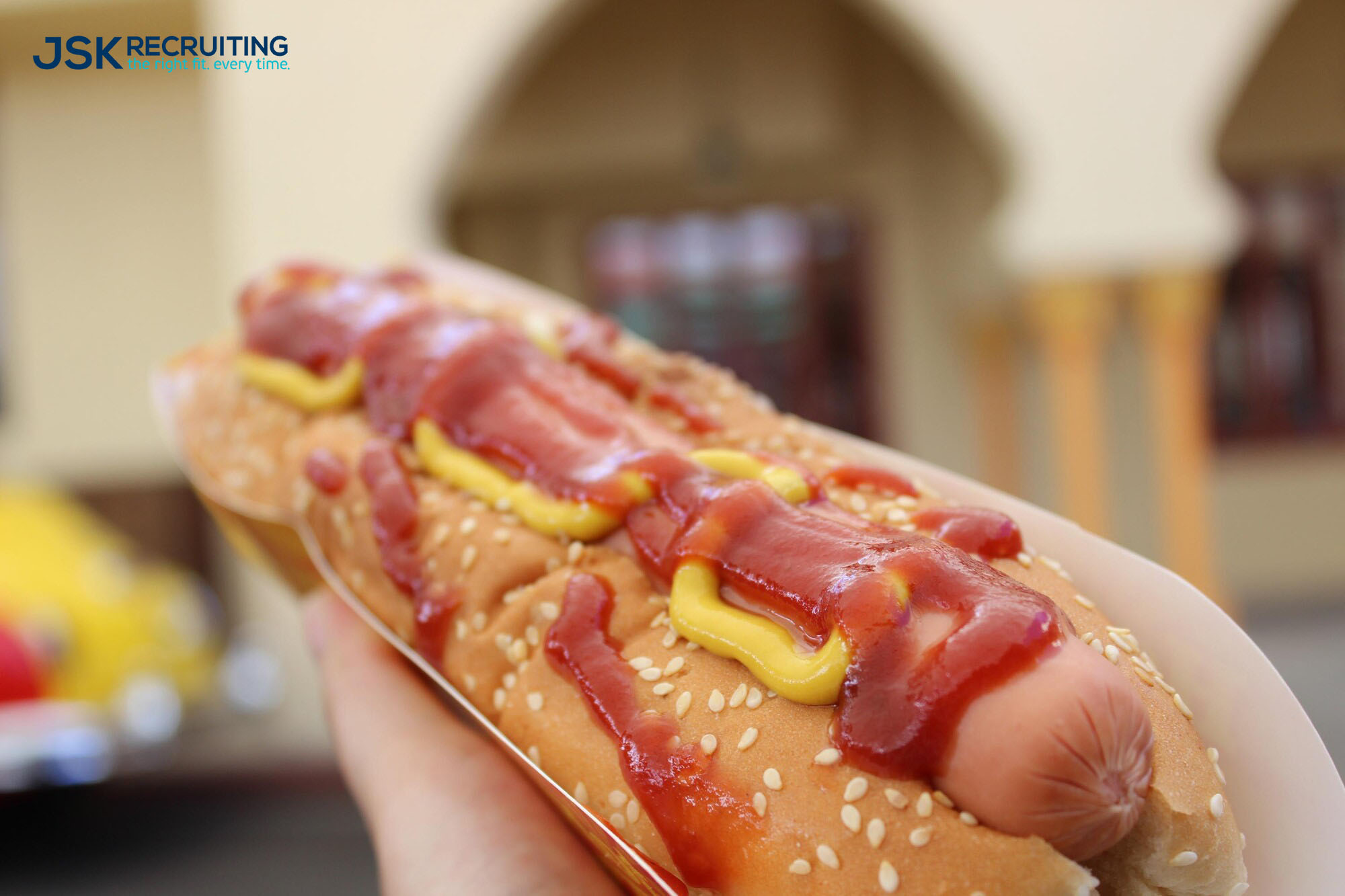 A person holding a hot dog with ketchup and mustard.