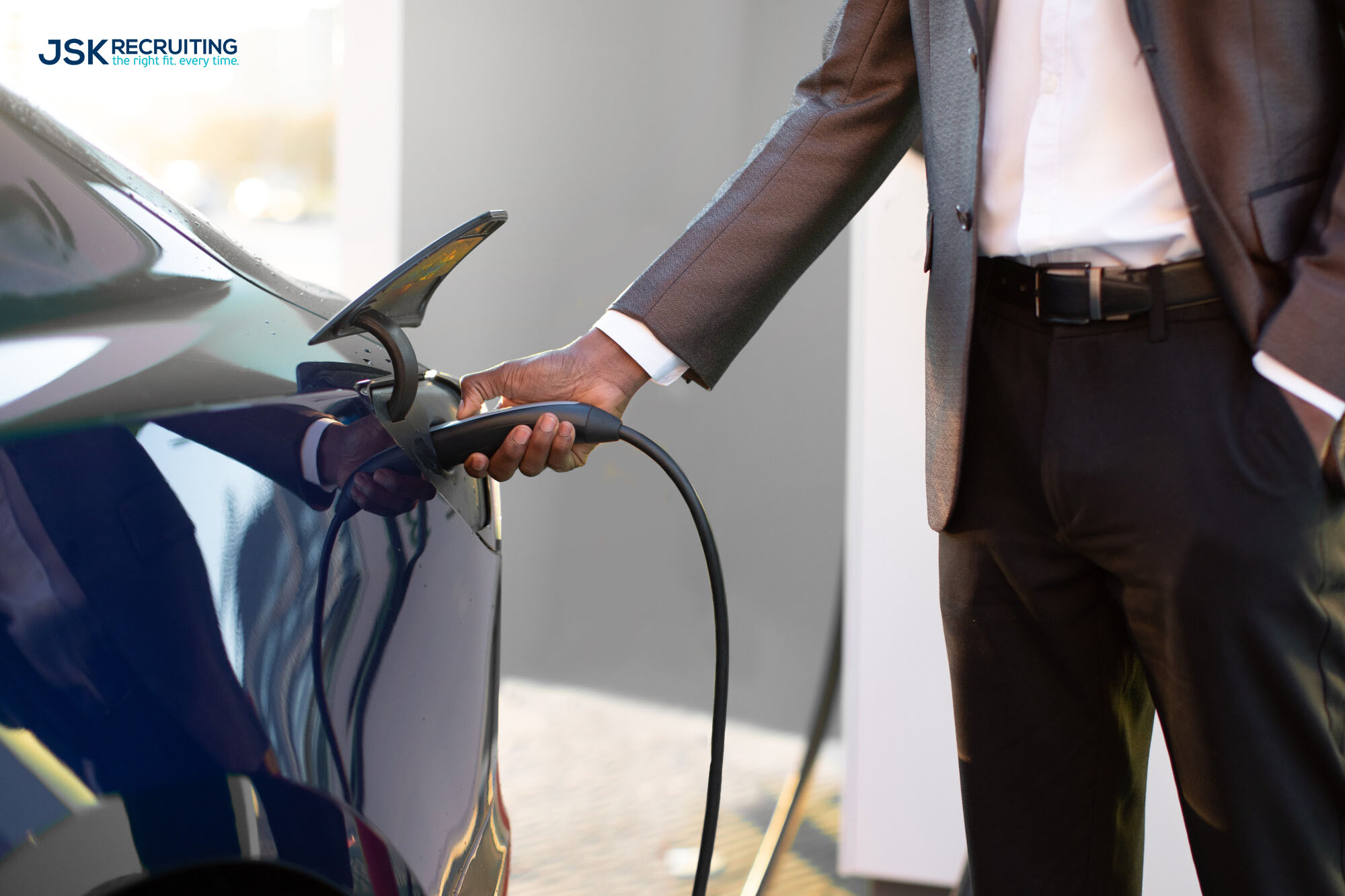 A man in suit and tie holding onto the handle of an electric car.