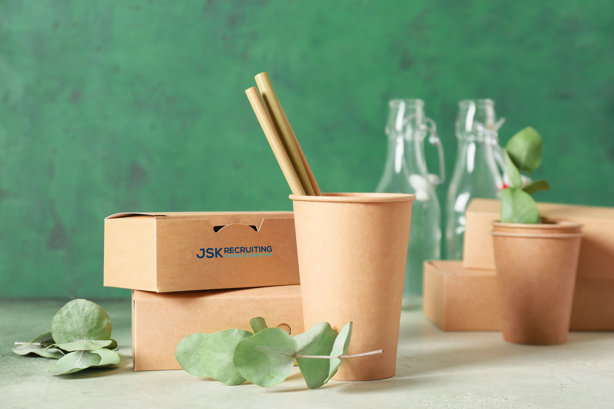 Eco cardboard containers for food and drinks on color background emblazoned with the JSK Recruiting logo.