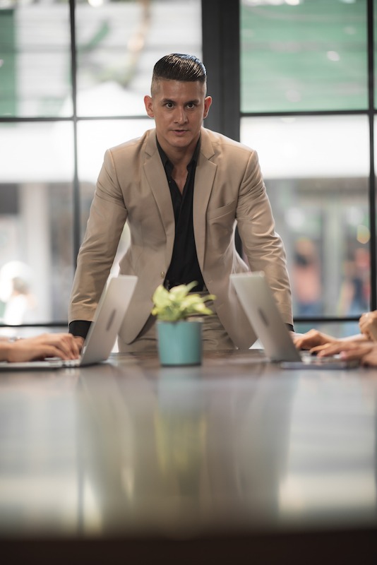 Business manager seriously leans forward on a conference table as he leads a meeting.