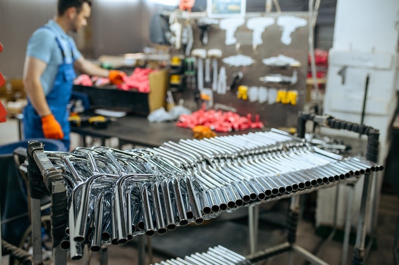 Factory employee works in the background behind a row of bicycle handlebars at a bicycle manufacturing plant.