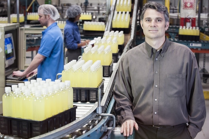 A factory manager stands next to yellow bottles on a conveyor belt in a bottling plant.