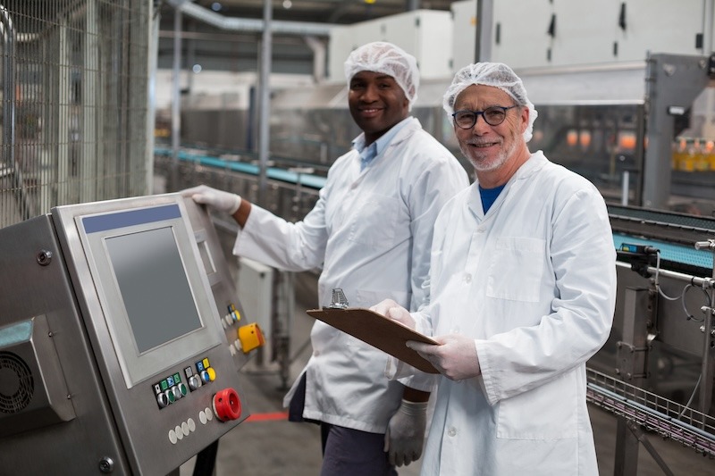 Two factory engineers in lab coats smile next to a machine in a food manufacturing plant.