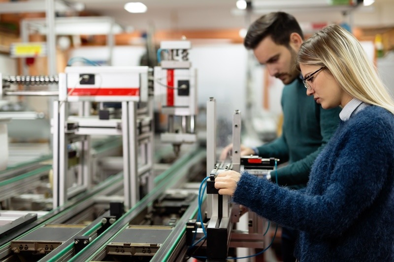 Two young well-dressed engineers adjust equipment in a fast-moving consumer goods factory.